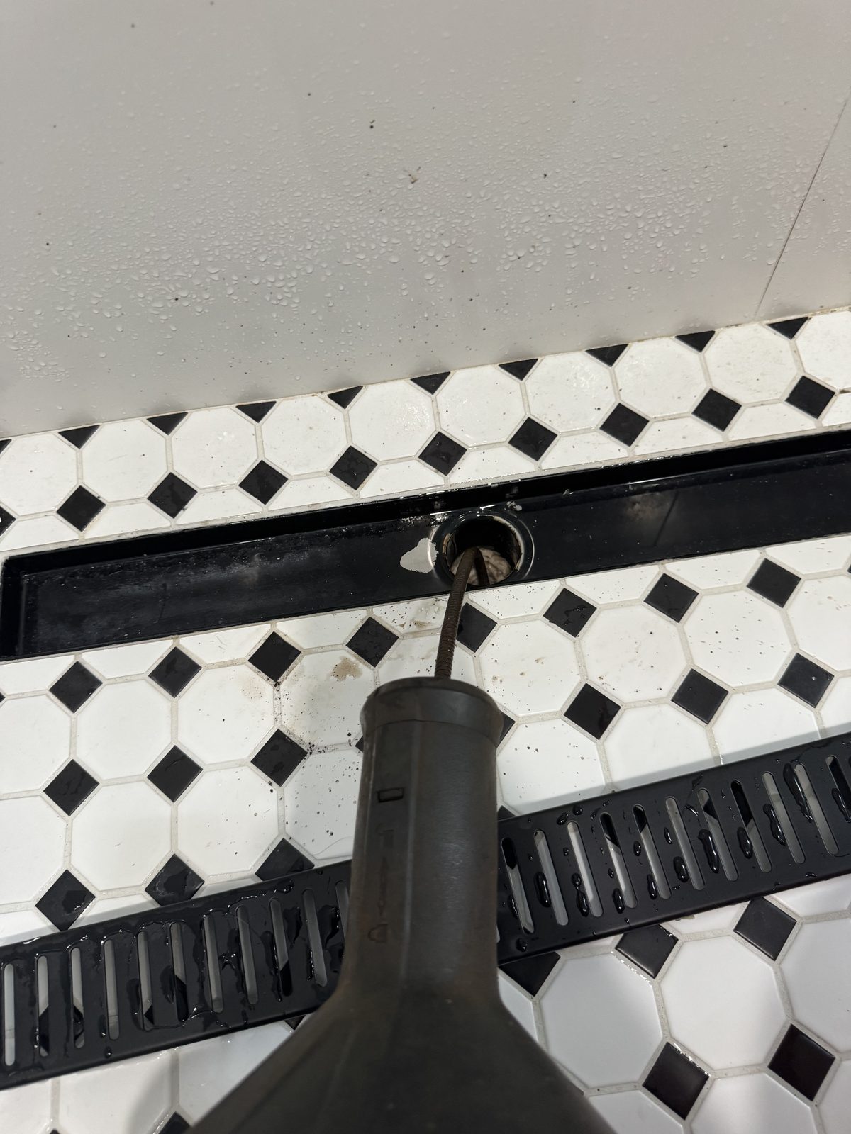 Clearing a clogged linear shower drain on a black-and-white tile bathroom floor in Cape Coral, FL.