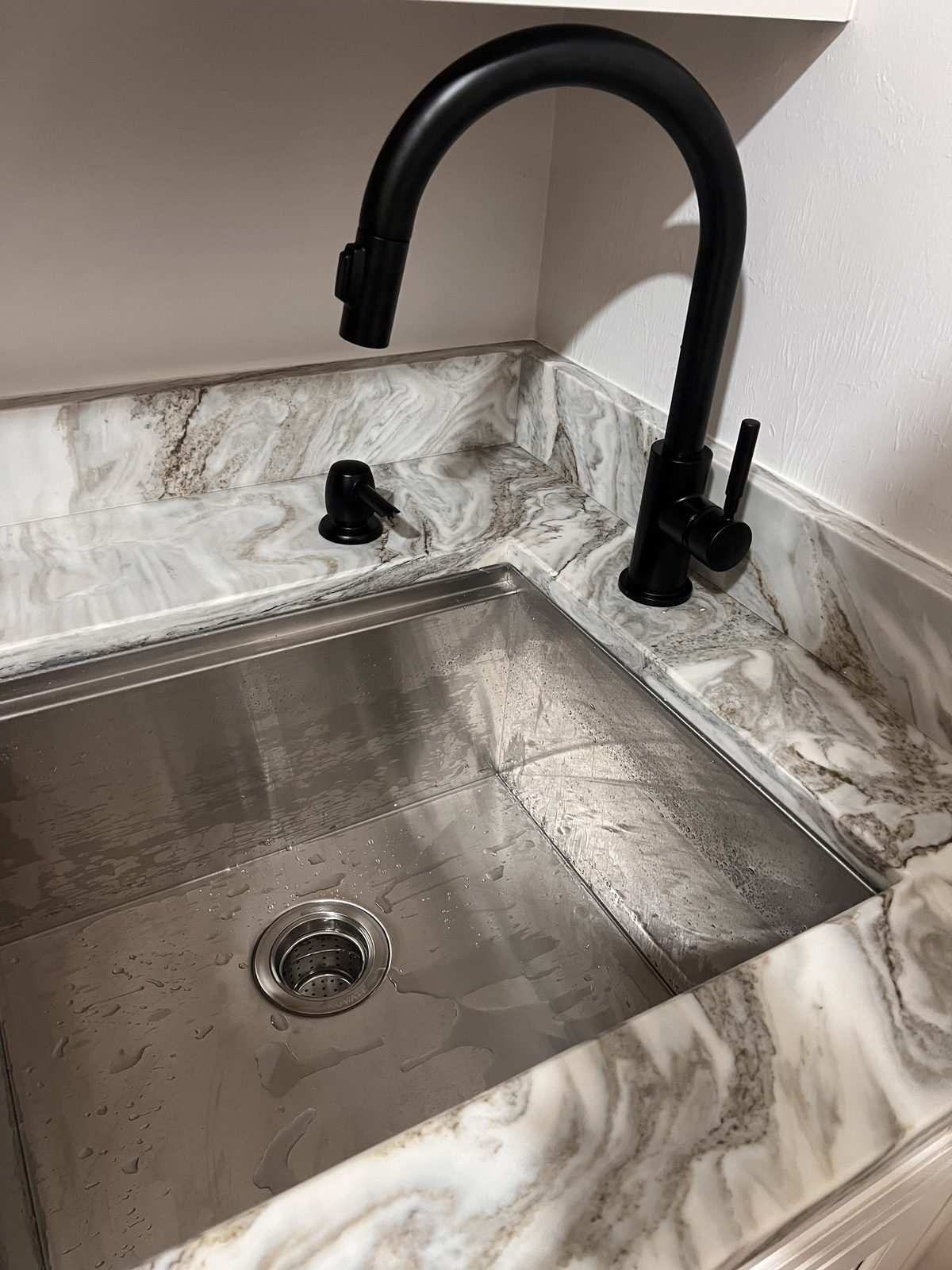Newly installed matte black pull-down kitchen faucet over a stainless undermount sink with marble counter in Cape Coral, FL.