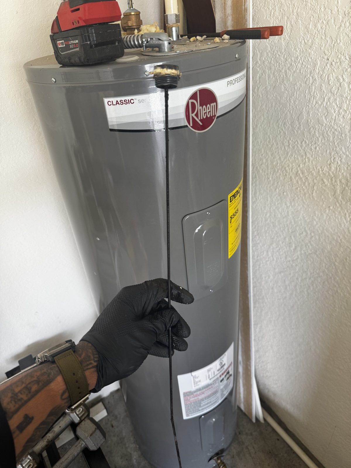 Plumber removing a corroded anode rod from a Rheem electric water heater during maintenance in Cape Coral, FL.